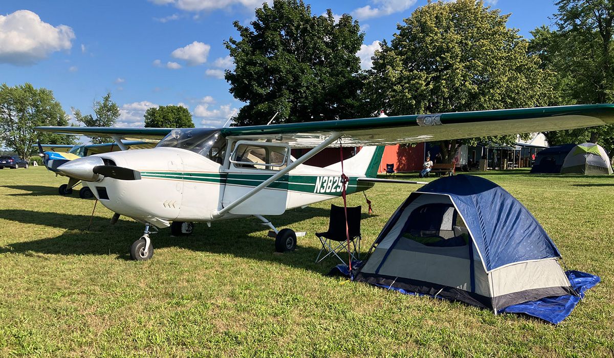 cessna 182 parked on grass with tent under the wing